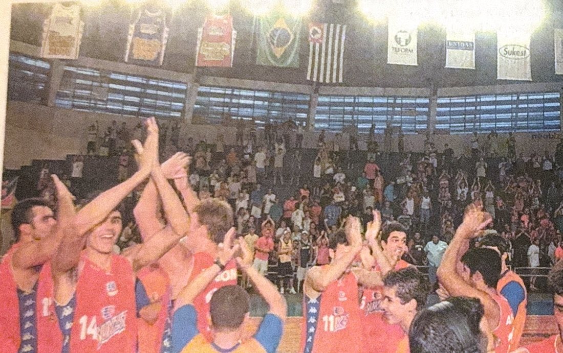 Jogadores de camisa laranja aplaudindo a torcida no ginásio lotado
